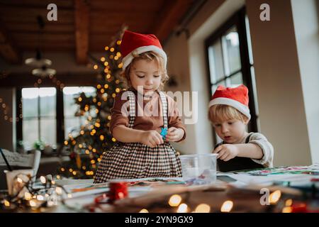 Fratelli che preparano biglietti natalizi per la famiglia. I bambini dipingono quadri per Babbo natale o realizzano decorazioni natalizie con acquerelli. Foto Stock