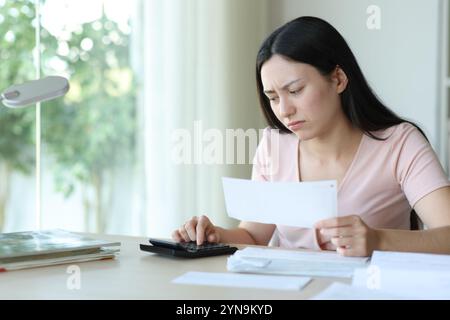 Donna asiatica preoccupata che calcolava le spese che tenevano la fattura a casa Foto Stock