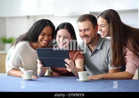 Quattro felici amici interrazziali che usano un tablet in cucina a casa Foto Stock