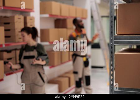 Attenzione selettiva agli scaffali pieni di scatole di cartone, in background diversi colleghi di magazzino che preparano gli ordini dei clienti. Dipendenti del magazzino che gestiscono il trasporto dei pacchi e lavorano nel magazzino Foto Stock