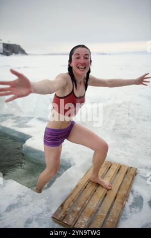 Una donna esce da una piscina nel lago ghiacciato Baikal durante l'inverno nell'isola di Olkhon, Siberia, Russia. Foto Stock