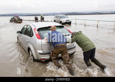 Uomini che spingono auto bloccati in un'inondazione a Storth, all'estuario del fiume Kent Foto Stock