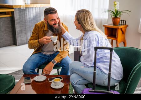 La giovane coppia felice va in vacanza. I turisti seduti nella hall dell'hotel bevono caffè. Foto Stock
