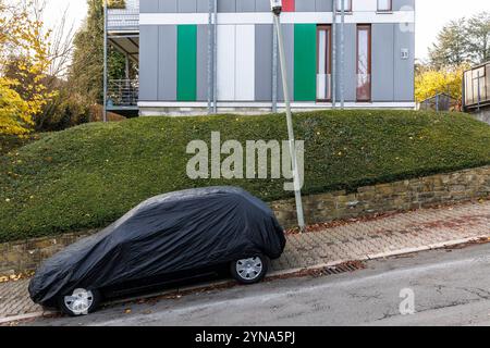 Un'auto coperta si trova su una strada in pendenza di fronte a una siepe a Wetter an der Ruhr, nell'area della Ruhr, nella Renania settentrionale-Vestfalia, Germania. eine abgedecktes Auto Foto Stock