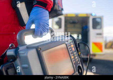 Servizio medico di emergenza. Primo piano della mano paramedica in guanti chirurgici blu mentre si corre con il monitor del defibrillatore contro l'auto dell'ambulanza. Temi r Foto Stock