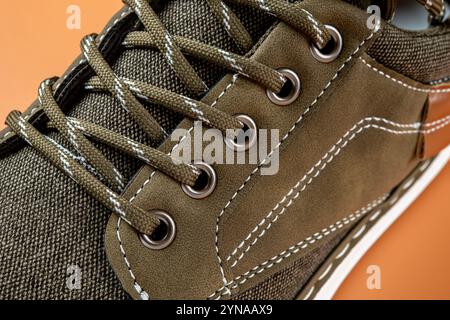 Lacci e occhielli di sneakers in tela kaki su sfondo arancione. Nuove scarpe in tessuto marrone con suola bianca per uno stile di vita attivo, camminare e correre. Foto Stock