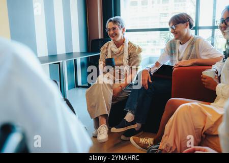 Un insegnante maturo condivide una pausa caffè con gli studenti durante una discussione in aula rilassata, promuovendo un ambiente di apprendimento confortevole in un ambiente moderno Foto Stock