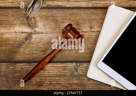 Il gavel del giudice poggia su una scrivania in legno accanto a un tablet PC digitale, un blocco note, suggerendo un ambiente professionale legale per le riunioni e le consultazioni. Foto Stock