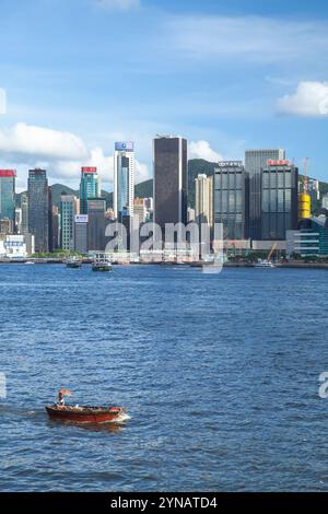 Hong Kong - 13 luglio 2017: Una piccola barca con un uomo sotto la umberella naviga sul mare di fronte al quartiere centrale della città di Hong Kong in un giorno d'estate Foto Stock