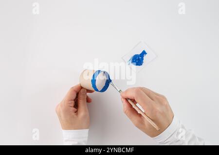 una persona che dipinge il bordo di un tubo di cartone con vernice blu utilizzando un pennello. Entra in un processo di creazione o fai da te, uso creativo di Ever Foto Stock