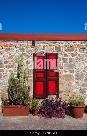 Vivaci persiane in legno dipinte di rosso montate su un muro di pietra tradizionale a Rodi Foto Stock