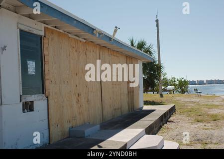 Vecchio edificio con finestre di copertura in compensato sul marciapiede sinistro che conduce le linee del muro del mare fuori dal porticciolo di Gulfport Florida alla Baia di Boca Ciega su un soleggiato Foto Stock