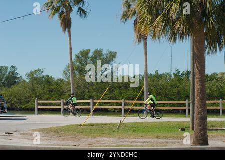 Uomo e donna in bicicletta da destra a sinistra nel mezzo vicino a Gulfport Marina Outlet che indossa abiti verdi fluorescenti e caschi. Recinzione in legno Foto Stock