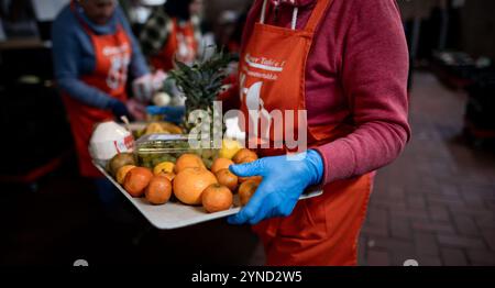 Oberhausen, Germania. 25 novembre 2024. Un dipendente porta frutta su un vassoio alla banca alimentare. Lunghe code davanti alla banca alimentare - e all'interno, volontari anziani e anziani che hanno urgente bisogno di nuove reclute e supporto. Molte banche alimentari in NRW stanno quindi suonando l'allarme. Alcuni hanno già chiuso a causa della mancanza di personale. Crediti: Fabian Strauch/dpa/Alamy Live News Foto Stock