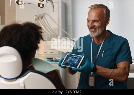 Dentista sorridente che mostra la radiografia dentale del paziente Foto Stock