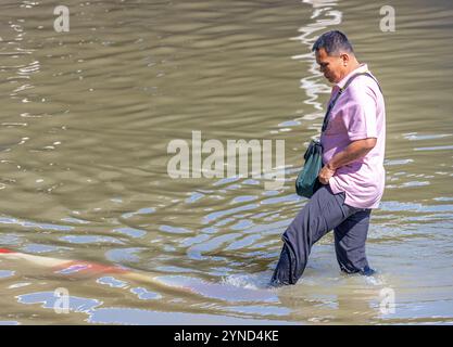 SAMUT PRAKAN, THAILANDIA, 19 novembre 2024, Un uomo attende con attenzione attraverso una strada allagata Foto Stock