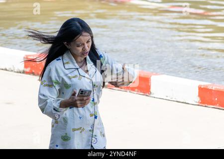 SAMUT PRAKAN, TAILANDIA, 19 novembre 2024, Una donna con capelli fluenti sta chiamando dal telefono sulla strada mattutina Foto Stock