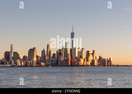 La parte meridionale dello skyline di Manhattan durante il tramonto. I grattacieli creano una silhouette accattivante con riflessi dorati che mettono in risalto la vita urbana. Foto Stock