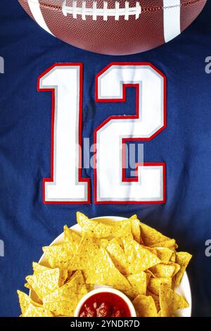 Un calcio americano con chip nacho organici e salsa delicata su una maglia da calcio blu bianca con il numero 12 in vista verticale Foto Stock