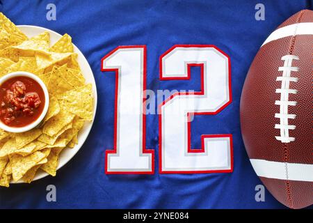 Un calcio americano con chip nacho organici e salsa dolce su una maglia da calcio blu bianco con il numero 12 in vista orizzontale Foto Stock
