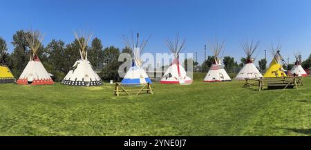 Calgary, Alberta, Canada. 14 luglio 2024. Una fila di coloratissimi tipidi sorge su un campo erboso, con un moderno paesaggio urbano visibile sullo sfondo Foto Stock