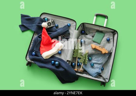 Valigia con abiti invernali, accessori da viaggio e decorazioni natalizie su sfondo verde. Vista dall'alto Foto Stock