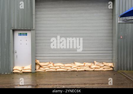 Sacchetti di sabbia impilati contro la porta a rulli di una fabbrica per evitare inondazioni dovute all'acqua inondabile in seguito a forti piogge provocate da una tempesta Foto Stock