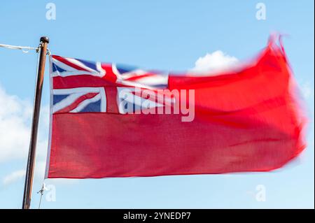 Una Red Ensign sfilacciata o bandiera Red Duster che sventola nella brezza contro un cielo blu, Falmouth, Regno Unito Foto Stock