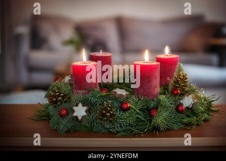 Terzo Avvento, corona verde con baule natalizie, biscotti alla stella alla cannella e candele rosse, tre sono accesi, su un tavolo nel soggiorno, spazio copia, se Foto Stock