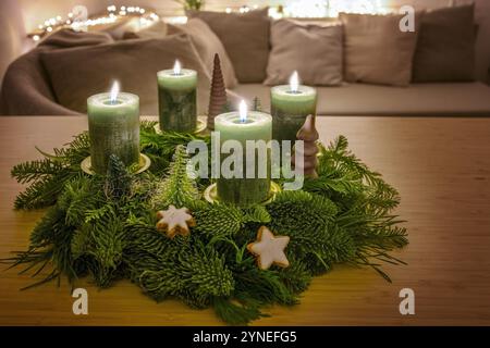 Quarto avvento, corona con quattro candele verdi accese e decorazioni natalizie su un tavolo in legno nel soggiorno, spazio copia, messa a fuoco selezionata, de stretta Foto Stock