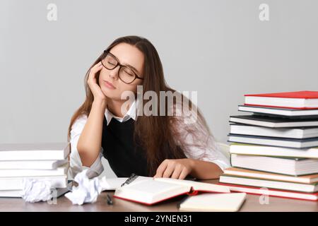 Giovane studente che soffre di stress prima dell'esame alla scrivania su sfondo grigio Foto Stock