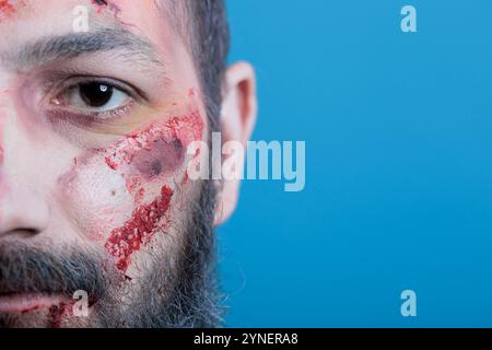 Ritratto di un uomo ferito pieno di sangue, vittima di bullismo, che si sente indifeso. Primo piano di occhi neri e cicatrici sulla persona ferita, concetto di problemi sociali, isolato sullo sfondo dello studio Foto Stock