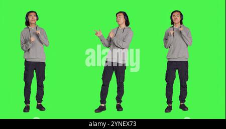 Persona che ascolta musica e balla con la fotocamera con le cuffie audio, divertiti con le canzoni e le mosse di danza funky. Un ragazzo positivo che si sente ottimista e felice, con sfondo "full body greenscreen". Foto Stock