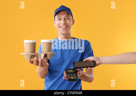 Operaio del fast-food che riceve il pagamento dal cliente tramite terminale su sfondo arancione, primo piano Foto Stock