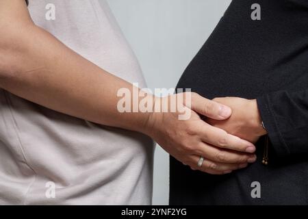 Coppia musulmana incinta non identificata che si tiene in piedi indossando abiti da donna neri e magliette da uomo color crema, romantico futuro padre e mot Foto Stock