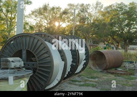 Tre bobine in metallo nero per il filo in un campo di linea diagonale durante i lavori di costruzione di una sottostazione elettrica. Grande tubo arrugginito su erba verde behi Foto Stock