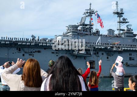 La famiglia e gli amici guardano i marinai e i marines man the rail mentre la nave d'assalto anfibia classe Wasp USS Boxer (LHD 4) torna alla base navale di San Diego, il 24 novembre 2024. I marinai assegnati alla nave d'assalto anfibio classe Wasp USS Boxer (LHD 4) e imbarcati sui Marines assegnati alla 15th Marine Expeditionary Unit tornarono a casa a San Diego dopo uno schieramento di cinque mesi nelle aree di operazione della 7th e della 3rd Fleet. (Foto della Marina degli Stati Uniti di Evan Diaz, specialista della comunicazione di massa di seconda classe) Foto Stock