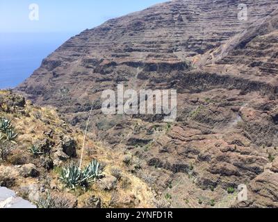 Le aspre scogliere rivelano una costa mozzafiato con profonde acque blu sottostanti. Il sole splende brillantemente sul terreno roccioso, mostrando una vegetazione variegata Foto Stock