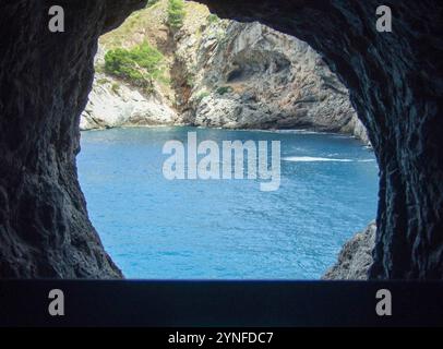 Attraverso una formazione rocciosa naturale, una vista mozzafiato rivela acque cristalline e vivaci scogliere costiere. La luce del sole si riflette sul mare calmo, creato Foto Stock
