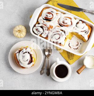 Dolci alla cannella o cannabon con tazza di caffè, ricoperti di glassa bianca sul piatto e piatto da forno su sfondo bianco. vista dall'alto Foto Stock