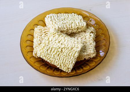 Spaghetti istantanei crudi su un piatto di vetro su una superficie di legno. Foto Stock