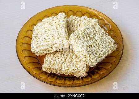 Spaghetti istantanei crudi su un piatto di vetro tenuto su una superficie di legno. Foto Stock