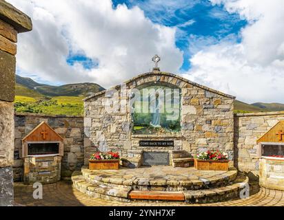 Un tranquillo santuario in pietra situato in un lussureggiante paesaggio montano sotto un vibrante cielo blu. L'ambiente tranquillo è impreziosito da fiori colorati, che fanno di me Foto Stock