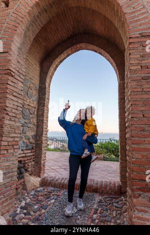 Madre con bambino in visita a un'antica fortezza musulmana al tramonto durante un tour panoramico. Madre che porta il suo bambino sotto un arco in una M antica Foto Stock