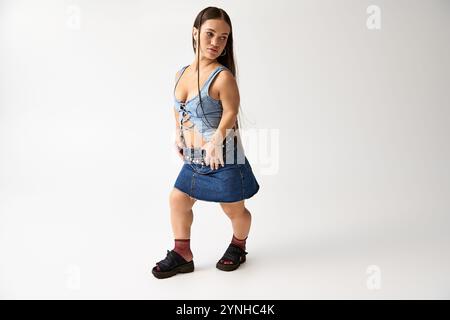 Una giovane donna elegante e di statura corta indossa con sicurezza un outfit di tendenza in denim. Foto Stock