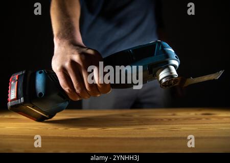 Una mano che afferra saldamente una fresa multiuso per utensili elettrici appoggiata su una superficie in legno, illuminata in modo drammatico dall'illuminazione artistica Foto Stock