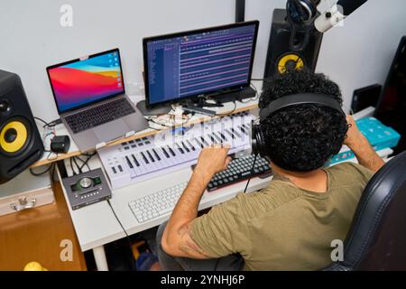 set di un compositore latino che compone una canzone a casa con un pianoforte e due monitor Foto Stock