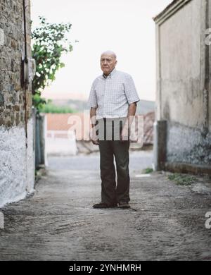 Un uomo anziano si trova contemplativamente in un vicolo stretto mentre la luce serale proietta ombre. L'atmosfera tranquilla mette in risalto il fascino rustico del sur Foto Stock