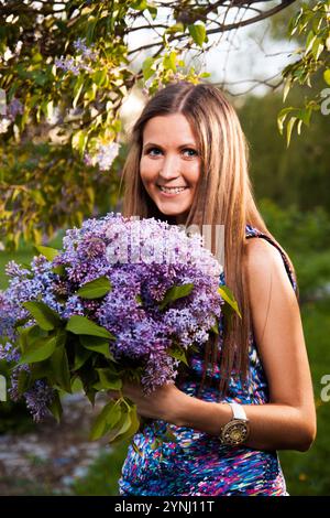 Moda giovane donna con fiori lilla in un giardino Foto Stock