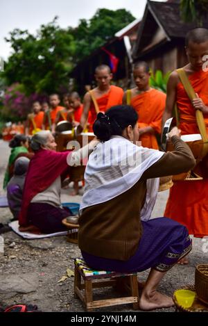 I fedeli fiancheggiano le strade e offrono cibo ai monaci di passaggio ogni mattina al Tak Bat, una cerimonia buddista millenaria a Luang Prabang, Laos Foto Stock